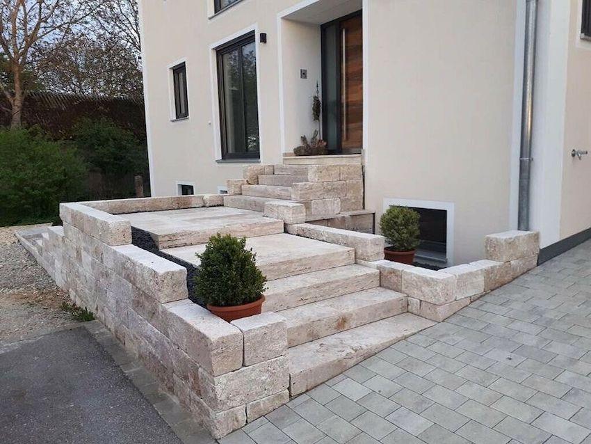 Blockstufen aus Travertin Classic Beige als breite Außentreppe mit Podest und seitlichen Natursteinmauern vor einem Wohnhaus.
