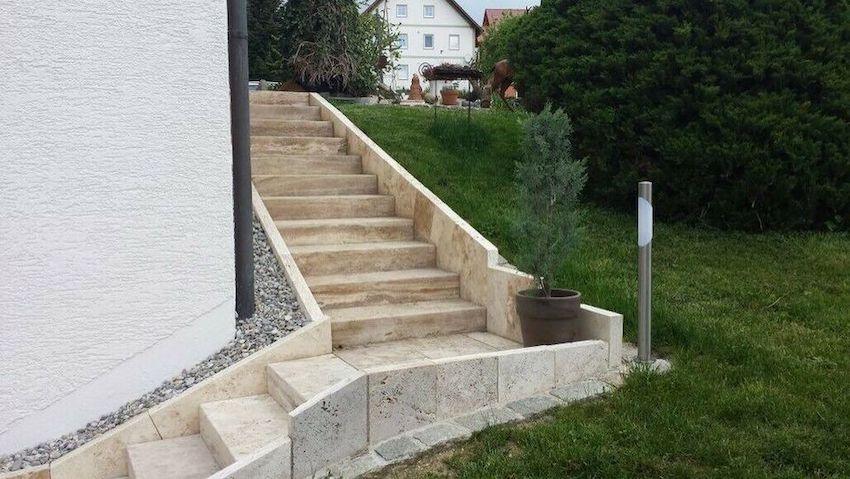 Blockstufen aus Travertin Classic Beige als lange Gartentreppe neben einer weißen Hauswand mit Natursteineinfassung.