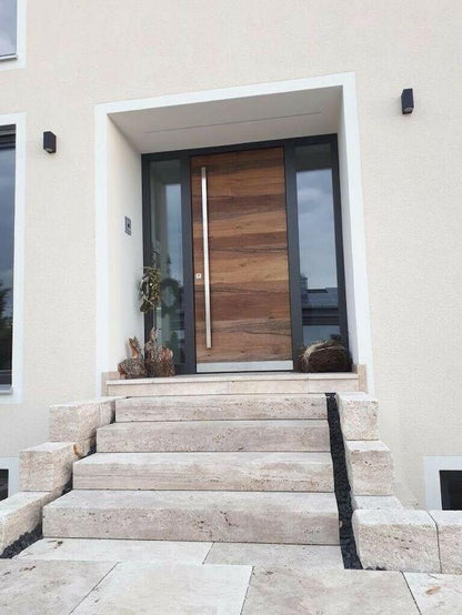 Blockstufen aus Travertin Classic Beige als Hauseingangstreppe vor einer Holztür mit seitlichen Glasflächen.